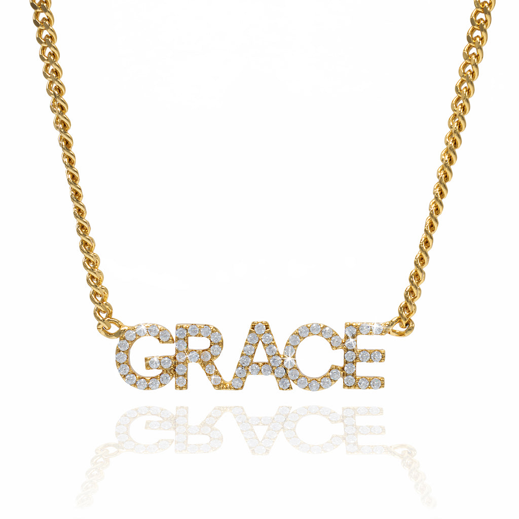 A gold-colored cuban custom name necklace with the name GRACE displayed on a reflective surface.
