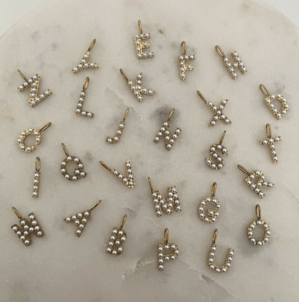 A-Z of pearl initial charms laid out on marble surface